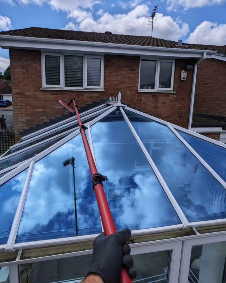 A conservatory roof being cleaned with a water fed pole. The roof is clean and shinning, reflecting the sky above like a mirror